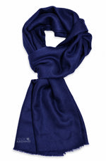A dark navy blue scarf with a soft, silky texture and fringed edges, styled in a loop on a plain white background. 